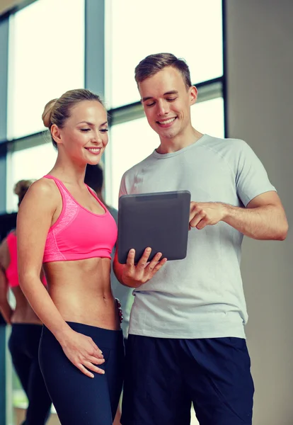 Spor salonunda kişisel antrenörüyle gülümseyen genç bir kadın. — Stok fotoğraf