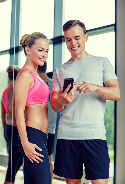 Smiling young woman with personal trainer in gym — Stock Photo, Image