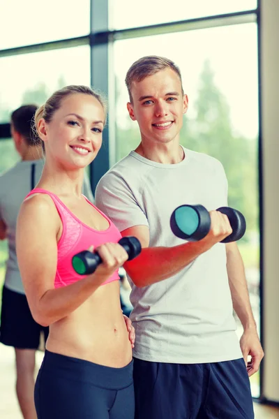 Smiling young woman with personal trainer in gym — Stock Photo, Image