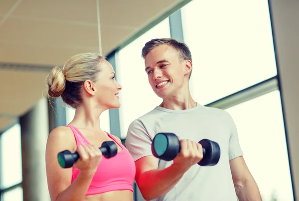 Spor salonunda kişisel antrenörüyle gülümseyen genç bir kadın. — Stok fotoğraf