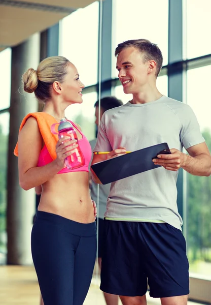 Spor salonunda kişisel antrenörüyle gülümseyen genç bir kadın. — Stok fotoğraf