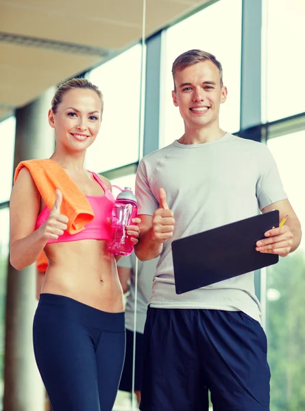 Leende ung kvinna med personlig tränare i gym — Stockfoto