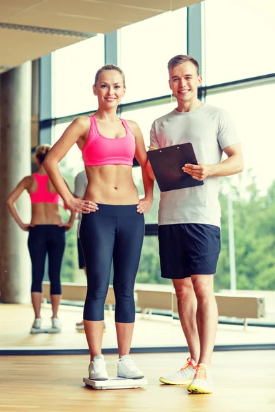 Lächelnder Mann und Frau mit Waage im Fitnessstudio — Stockfoto