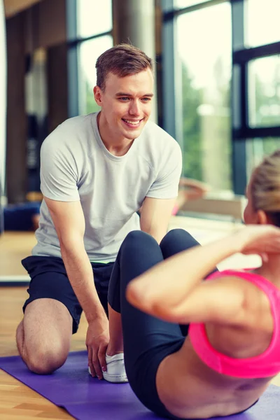 Mujer sonriente con entrenador masculino haciendo ejercicio en el gimnasio —  Fotos de Stock