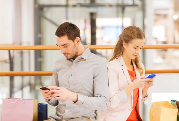 Пара со смартфонами и сумки в торговом центре — стоковое фото