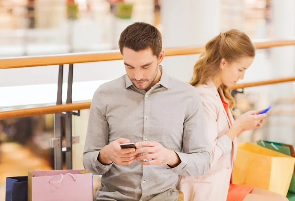 Pareja con smartphones y bolsas de compras en el centro comercial — Foto de Stock