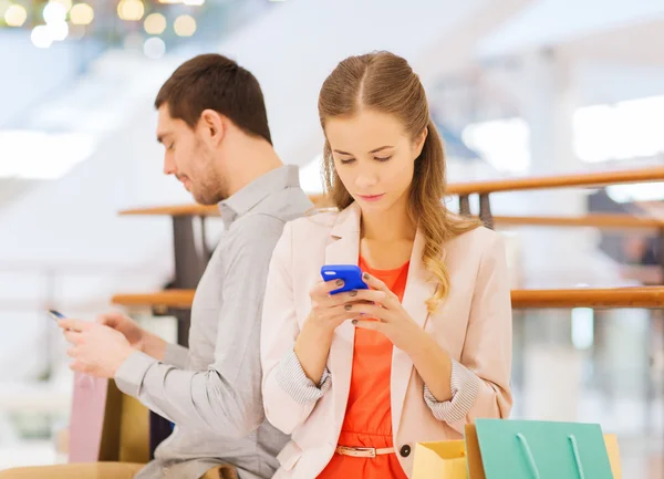 Casal com smartphones e sacos de compras no shopping — Fotografia de Stock