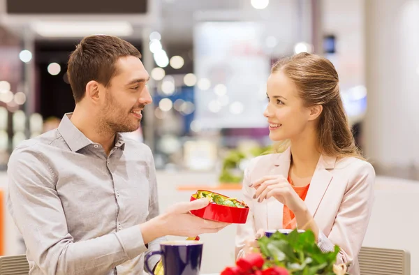 Happy couple with present and flowers in mall — Stock Photo, Image