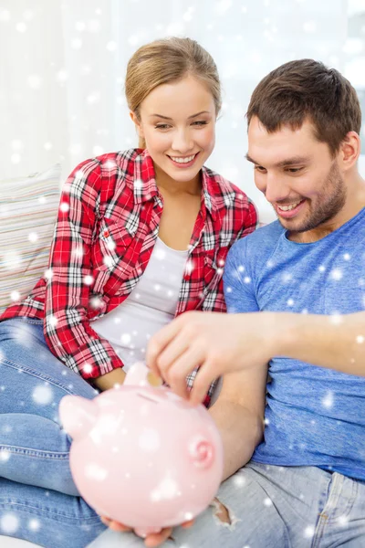 Smiling couple with piggybank sitting on sofa — Stock Photo, Image