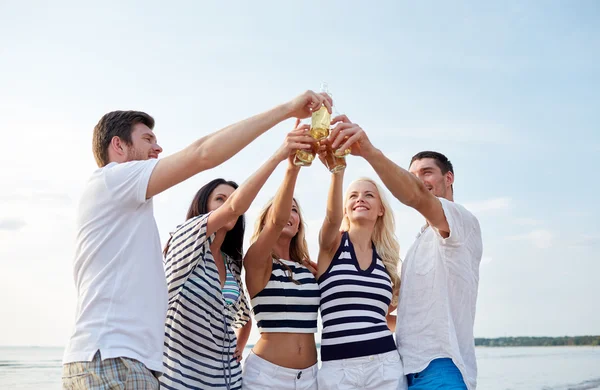 Smiling friends clinking bottles on beach — Stock Photo, Image