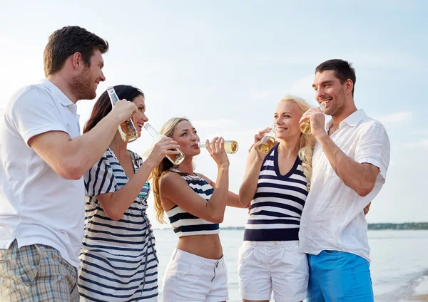 Lachende vrienden met dranken in flessen op strand — Stockfoto