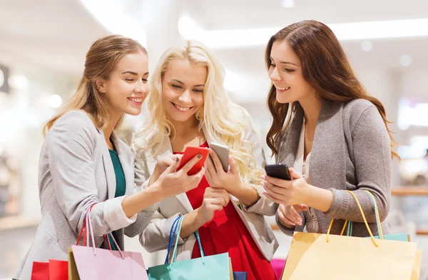 Glada kvinnor med smartphones och påsar — Stockfoto