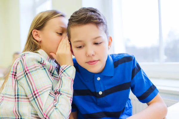 Smiling schoolgirl whispering to classmate ear — Stock Photo, Image