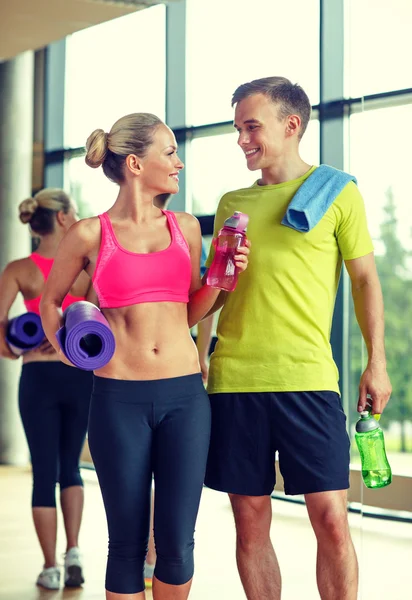 Pareja sonriente con botellas de agua en el gimnasio —  Fotos de Stock