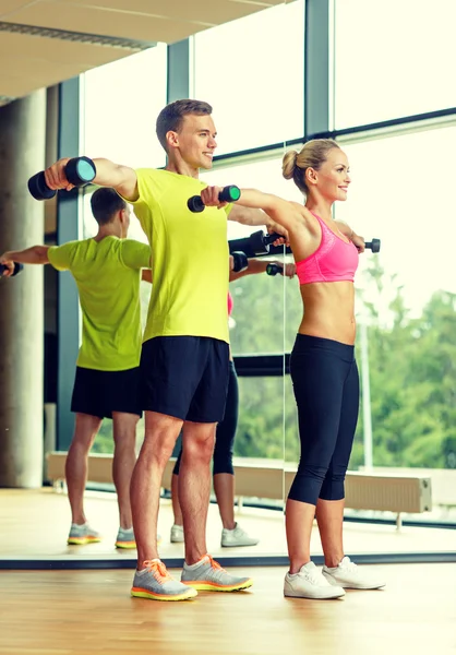 Uomo e donna sorridente con manubri in palestra — Foto Stock