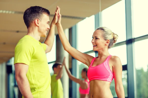 Sonriente hombre y mujer haciendo alta cinco en el gimnasio — Foto de Stock