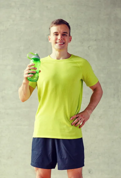 Hombre sonriente con botella de agua en el gimnasio — Foto de Stock