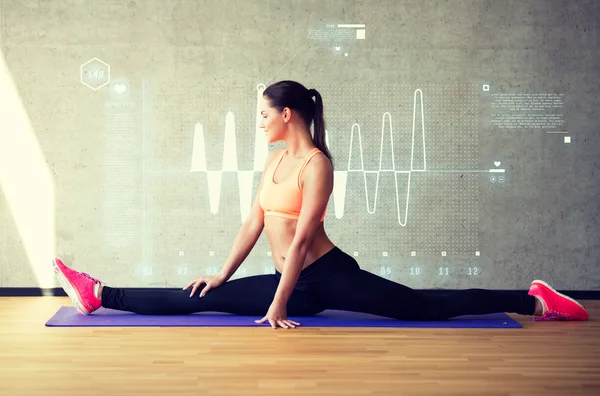 Leende kvinna sträcker benet på matta i gym — Stockfoto