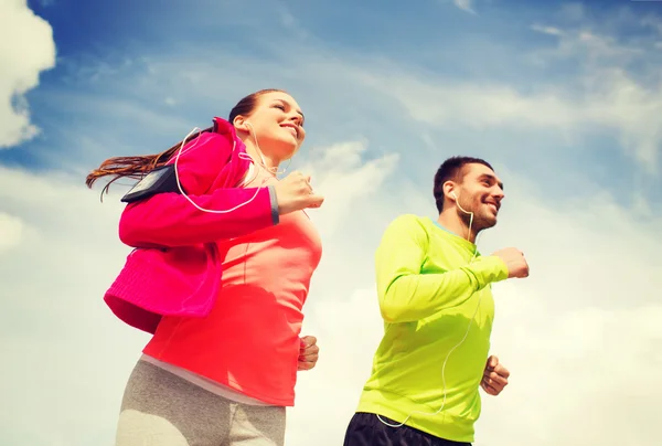 Sonriente pareja con auriculares corriendo al aire libre — Foto de Stock