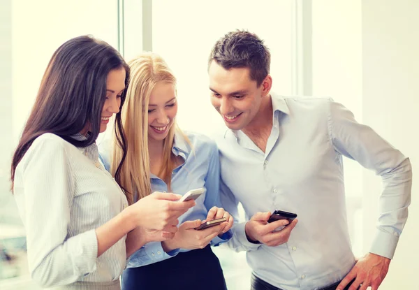 Equipe de negócios sorridente com smartphones no escritório — Fotografia de Stock