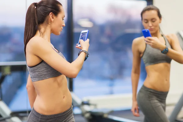 Woman with smartphone taking mirror selfie in gym — Stock Photo, Image