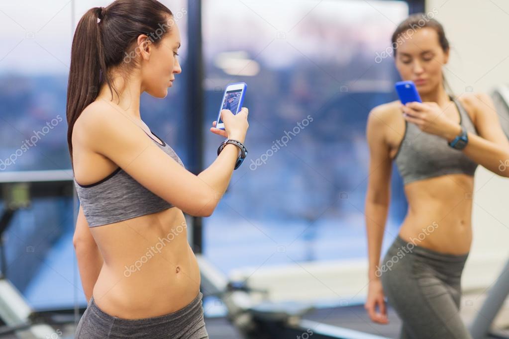 Woman with smartphone taking mirror selfie in gym — Stock Photo