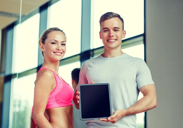 Smiling young woman with personal trainer in gym — Stock Photo, Image