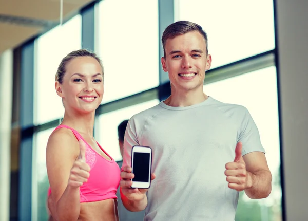 Giovane donna sorridente con personal trainer in palestra — Foto Stock