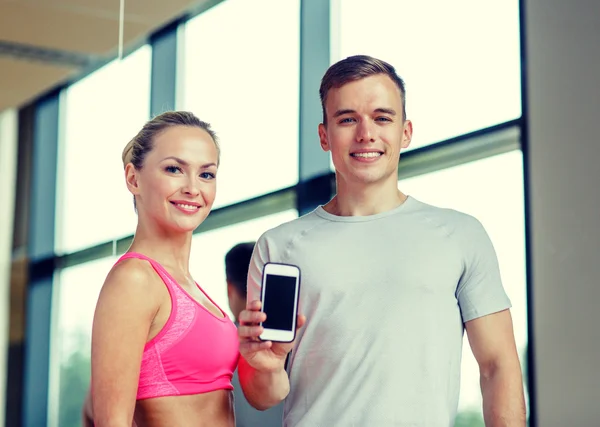 Smiling young woman with personal trainer in gym — Stock Photo, Image