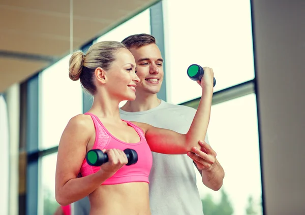 Sorrindo jovem mulher com personal trainer no ginásio — Fotografia de Stock