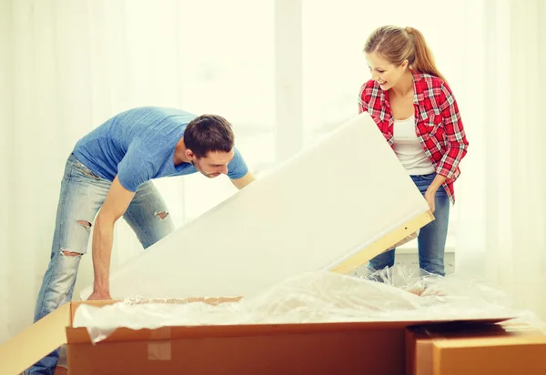 Smiling couple opening big cardboard box with sofa — Stock Photo, Image