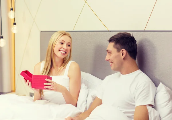 Lachende paar in bed met rode luxe-geschenketui — Stockfoto