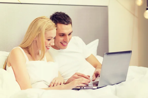 Pareja sonriente en la cama con ordenador portátil — Foto de Stock