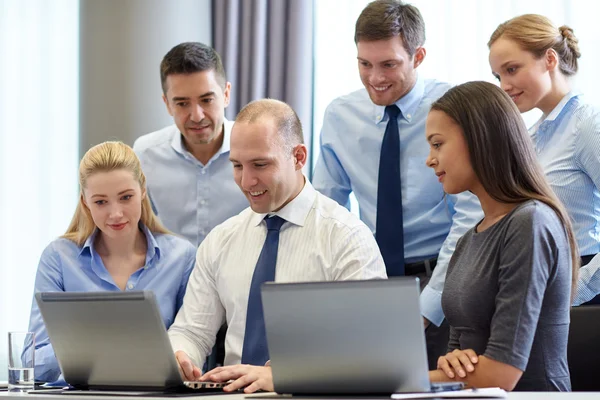 Uomini d'affari sorridenti con computer portatili in ufficio — Foto Stock