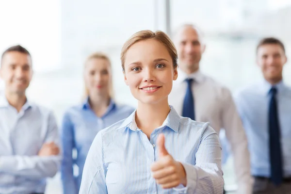 Sonriente mujer de negocios mostrando pulgares hacia arriba en la oficina —  Fotos de Stock