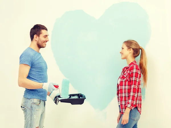 Smiling couple painting big heart on wall — Stock Photo, Image