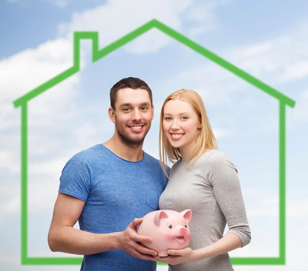 Smiling couple holding piggy bank over green house — Stock Photo, Image