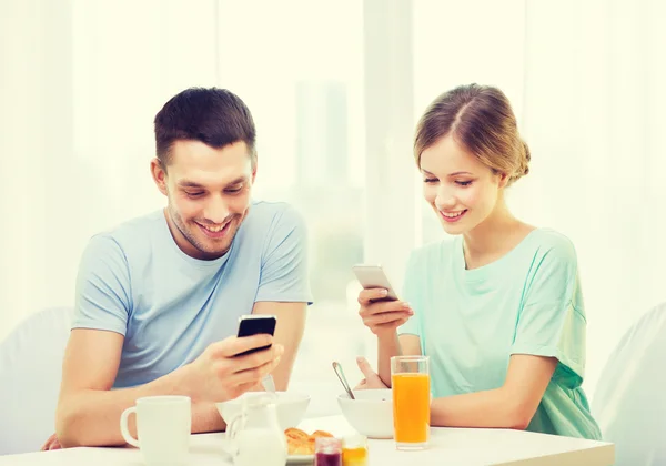 Casal sorridente com smartphones lendo notícias — Fotografia de Stock