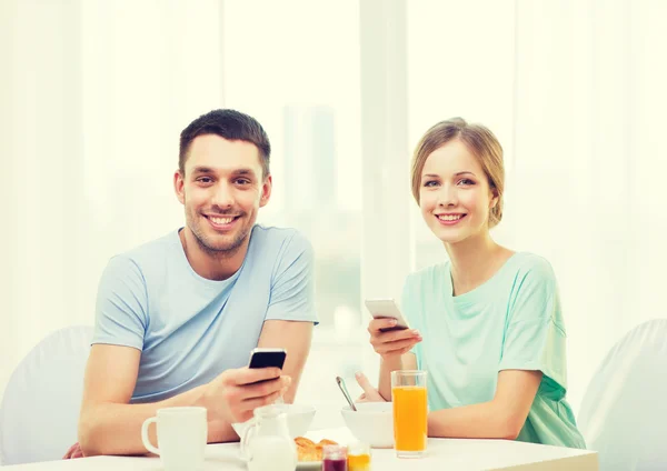 Casal sorridente com smartphones lendo notícias — Fotografia de Stock