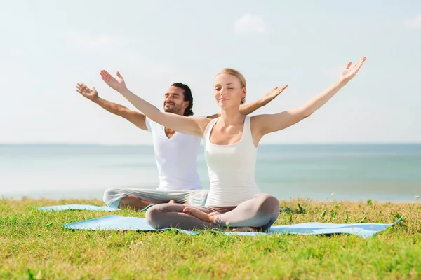 Pareja sonriente haciendo ejercicios de yoga al aire libre —  Fotos de Stock