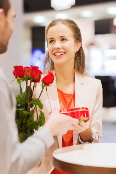 Gelukkige paar met heden en bloemen in winkelcentrum — Stockfoto