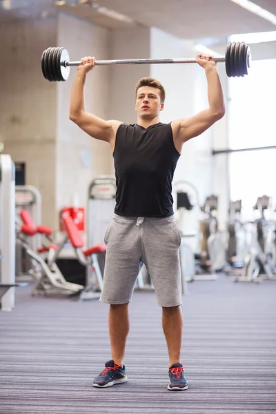 Jovem homem flexionando músculos com barbell no ginásio — Fotografia de Stock