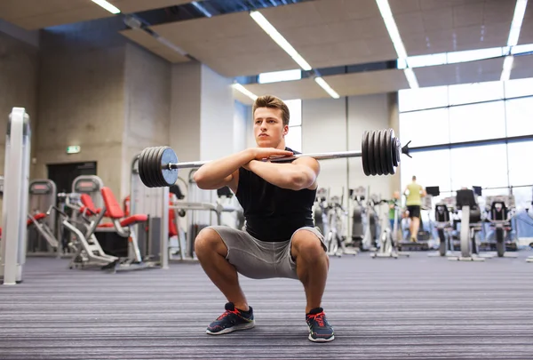 Joven hombre flexionando los músculos con barra en el gimnasio —  Fotos de Stock