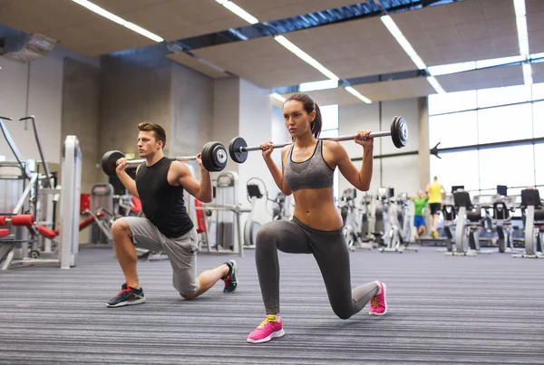 Jonge man en vrouw met barbell in gym training — Stockfoto