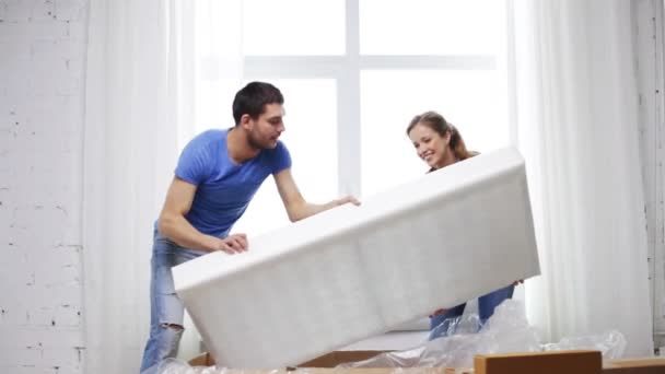 Улыбающаяся пара открывает большую картонную коробку с диваном — стоковое видео