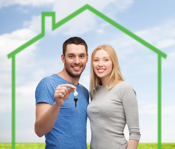 Casal sorrindo segurando chave sobre casa verde — Fotografia de Stock