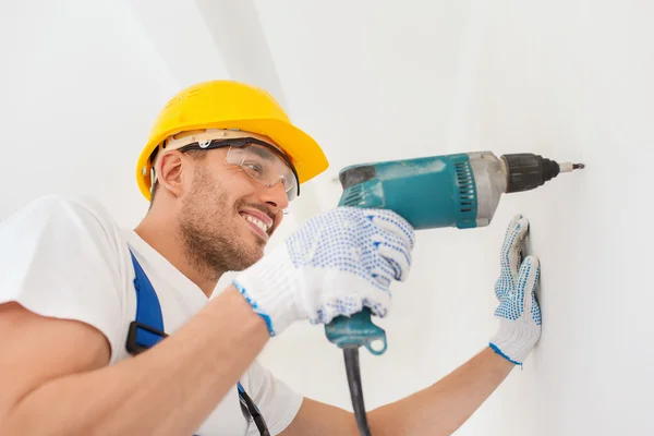 Smiling builder in hardhat drilling wall indoors — Stock Photo, Image