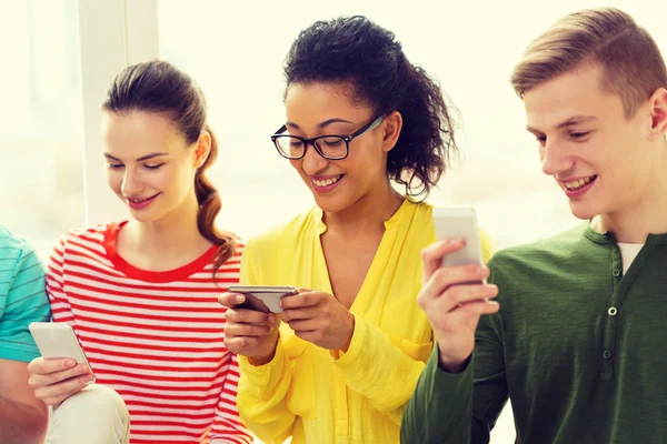 Tre studenti sorridenti con smartphone a scuola — Foto Stock