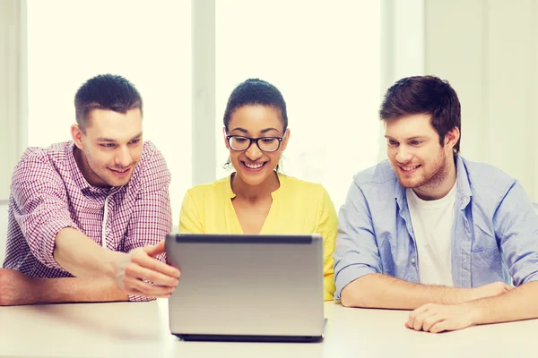 Tres colegas sonrientes con portátil en la oficina —  Fotos de Stock