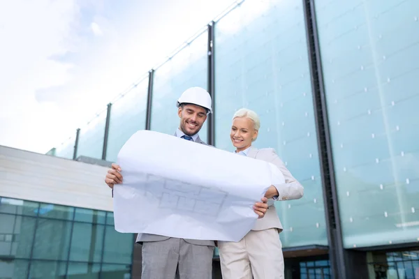 Glimlachende zakenmensen met blauwdruk en helmen — Stockfoto